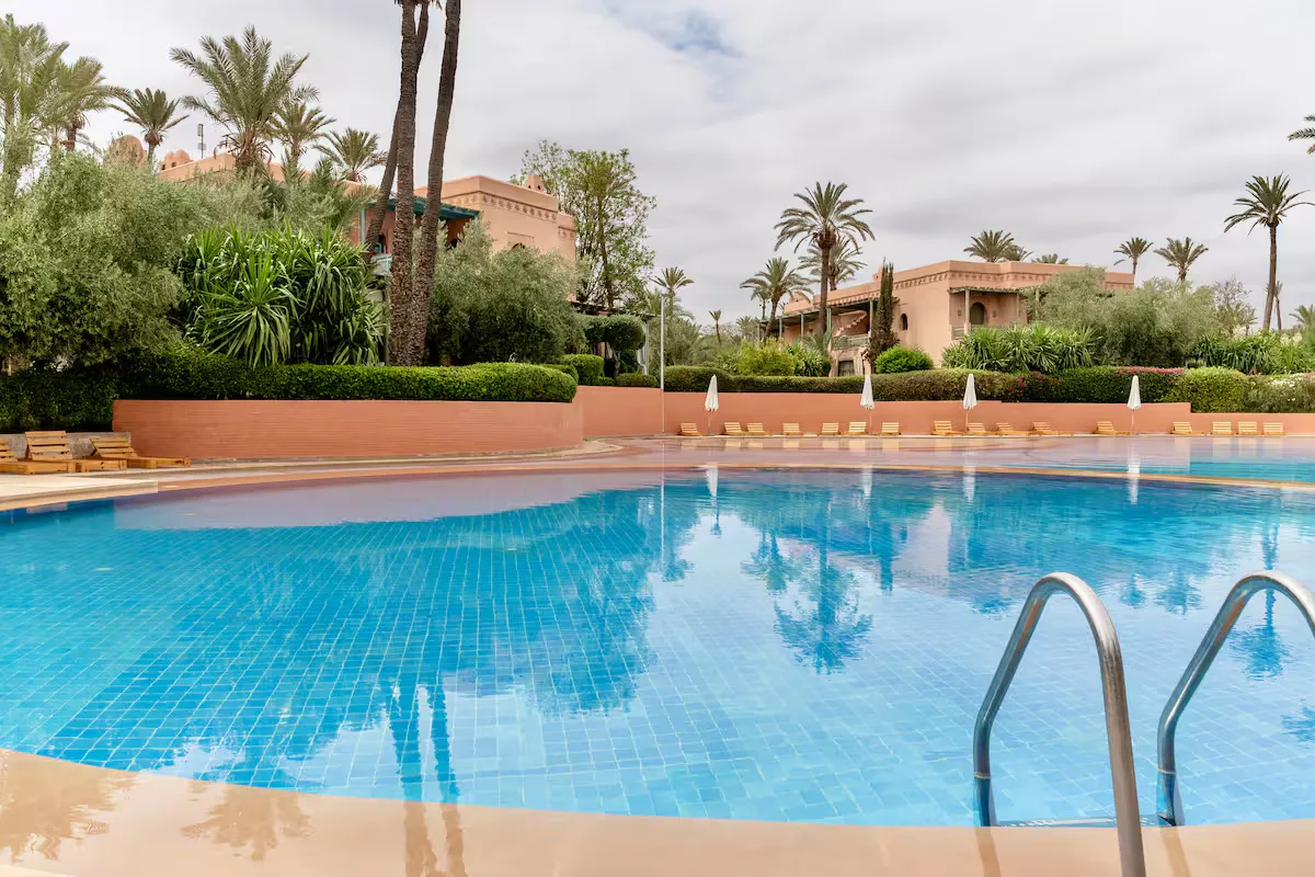 Close-up view of the swimming pool in a traditional-style Marrakech residence, with a metal ladder in the foreground and vintage apartment buildings in the background.