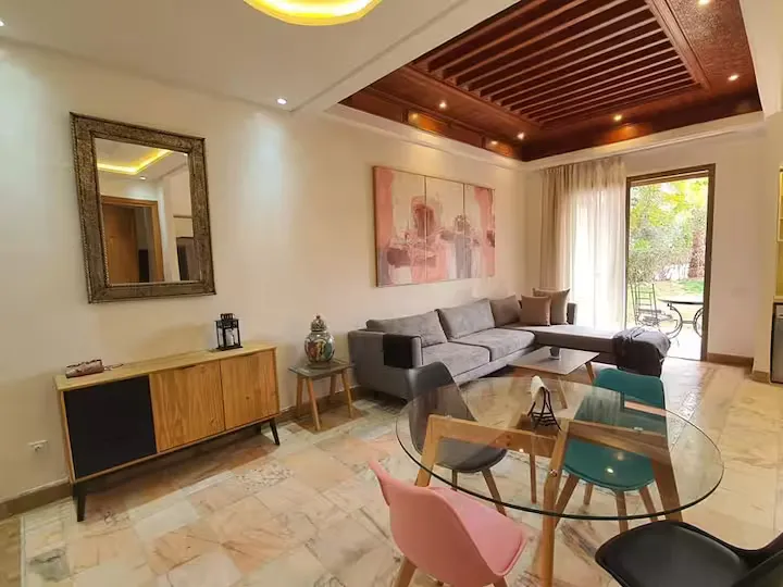Spacious living room with corner sofa, dining table, and wooden ceiling details in an apartment with pool in Marrakech