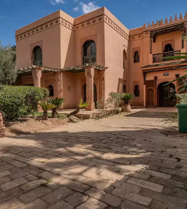 Traditional Moroccan ochre building facade surrounded by green gardens at an apartment with pool in Marrakech
