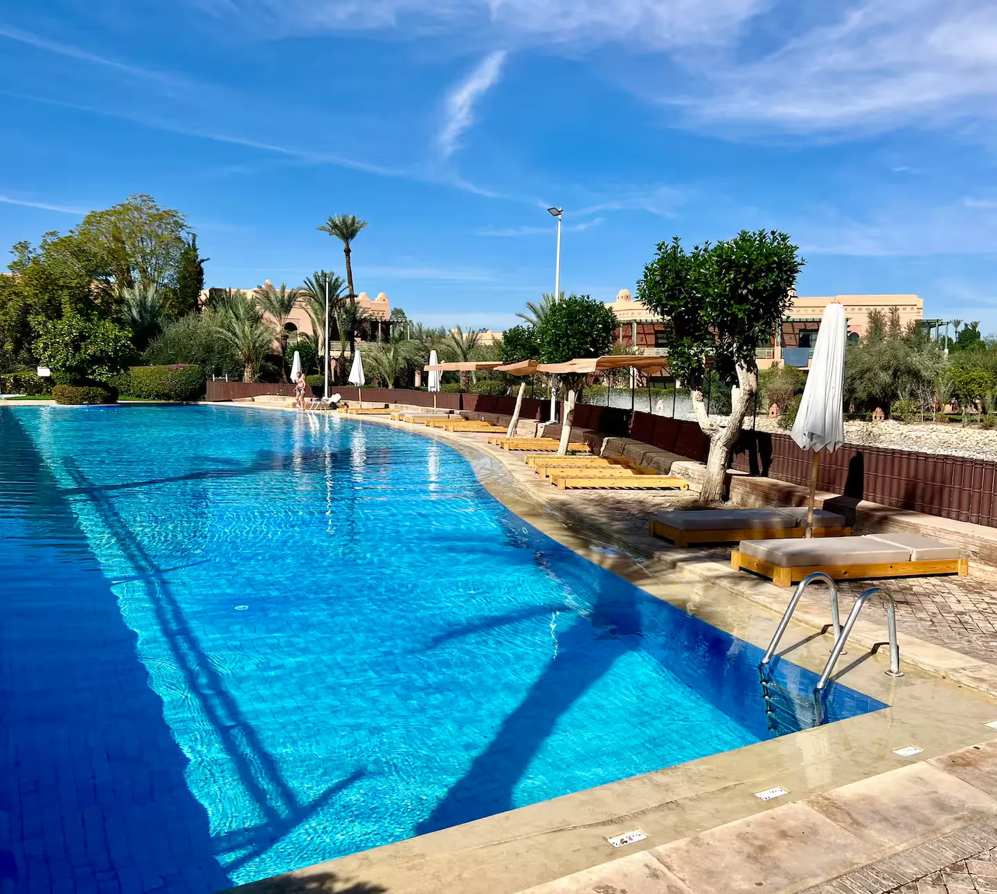 Large outdoor swimming pool with sunbeds and umbrellas in the residence of this apartment with pool in Marrakech