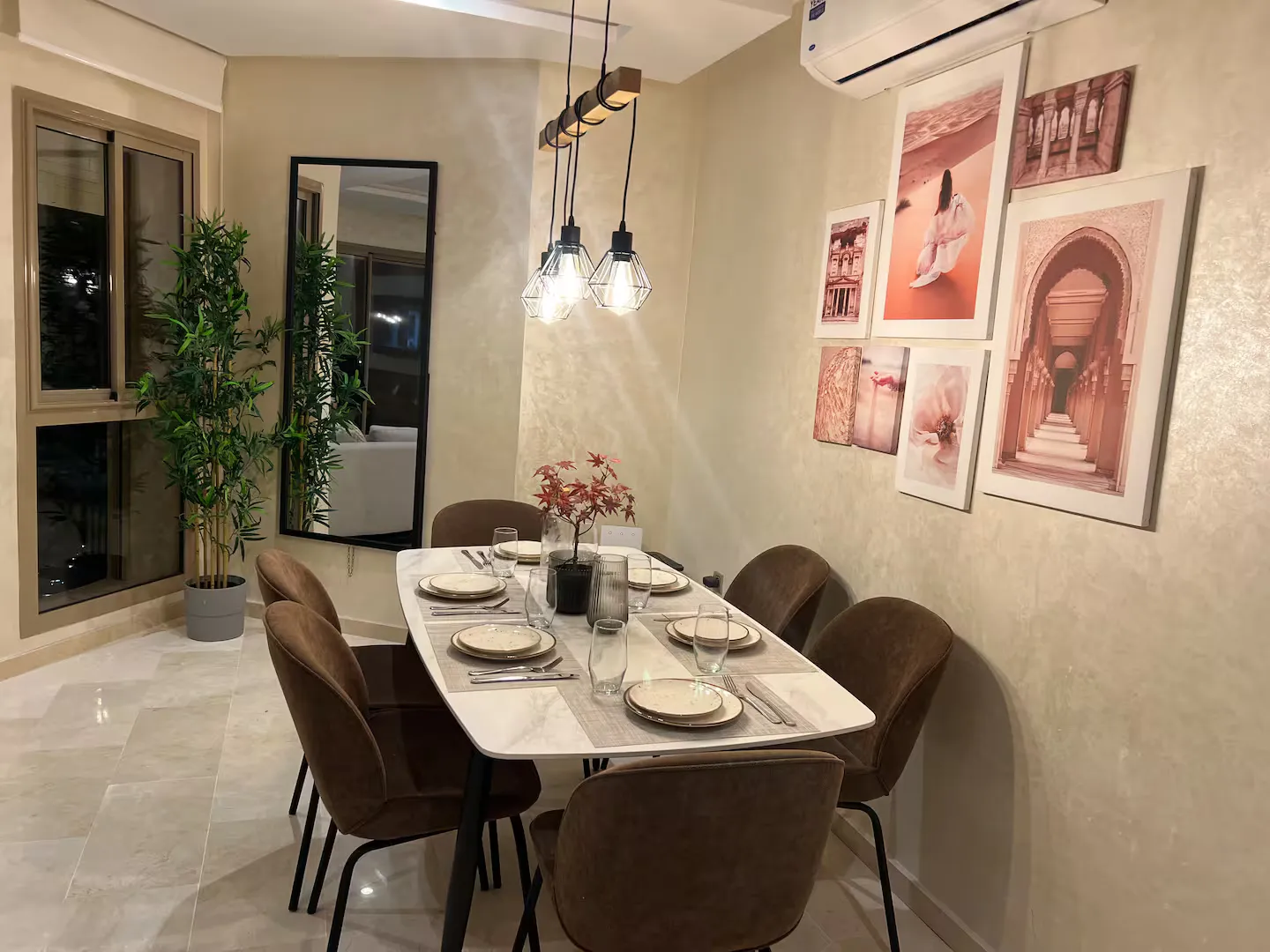 Warm dining area with a marble-style set table, velvet chairs, and modern pendant lights in a palm grove apartment