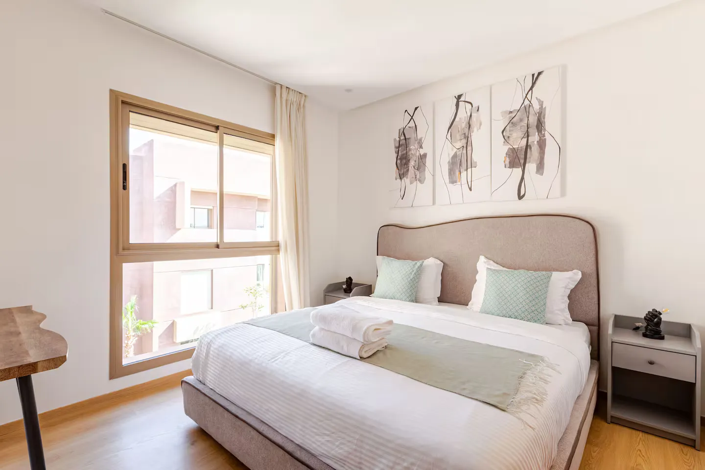 Second double bedroom with upholstered headboard, fresh linens, and large window in a palm grove apartment