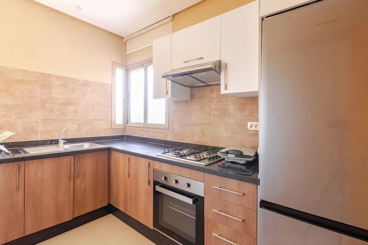 Alt : Fully equipped modern kitchen with oven, gas stovetop, and large fridge in a palm grove apartment